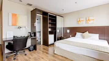 A hotel room with a bed, a desk with a chair, a wardrobe, and a bedside table.