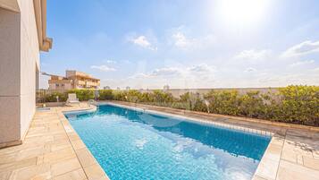 A swimming pool with tiled edges, a stone deck, and a view of buildings in the background.