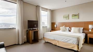 Habitación de hotel con una cama grande, un televisor sobre un mueble de madera, un escritorio y vistas a la ciudad.