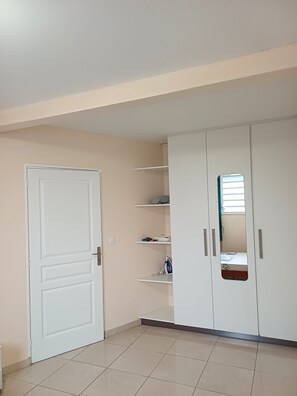 A room with a white door, a wardrobe with shelves, and a tiled floor. - Santa Marta - 2-Bedroom Apartment (Rivière-Pilote)