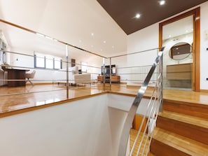 A spacious room with a high ceiling, a wooden floor, a staircase with a glass railing, and a large mirror on the wall. - Bravissimo Plaça Catalunya 10, Duplex Penthouse with 3 bedrooms (Girona)