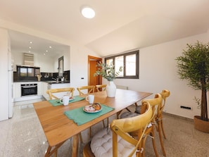 A dining area with a wooden table and chairs, a vase with green foliage, and a view of the kitchen and living space. - Bravissimo Plaça Catalunya 10, Duplex Penthouse with 3 bedrooms (Girona)
