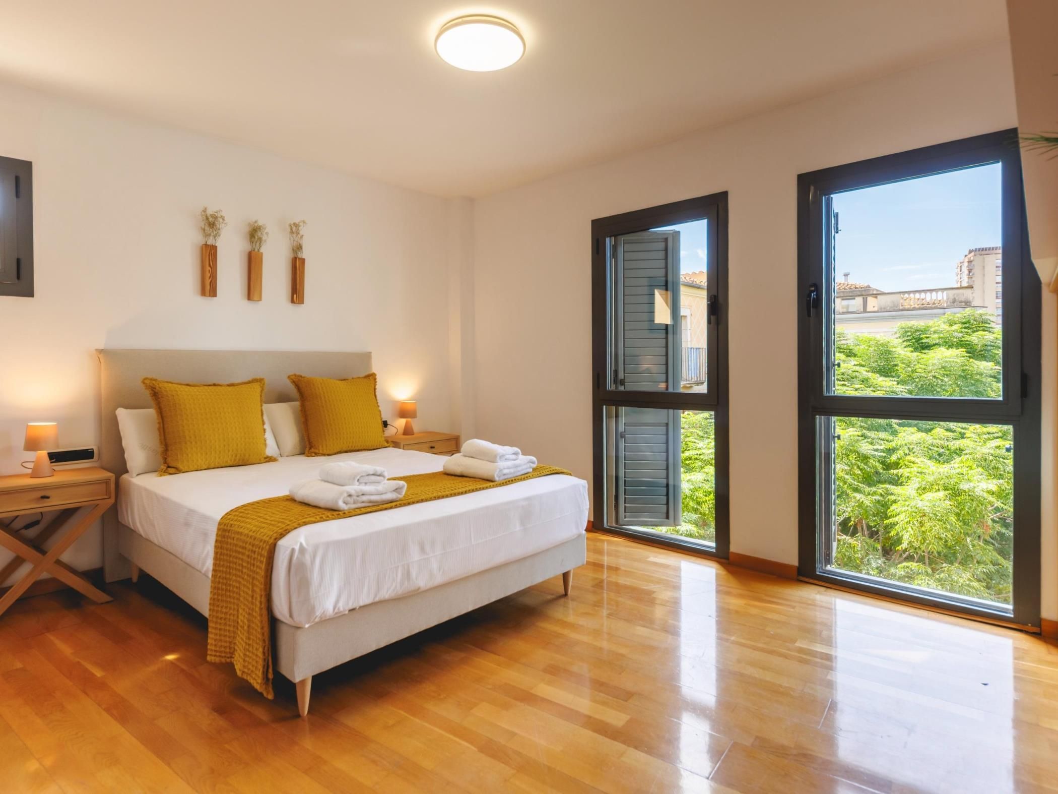A bedroom with a bed, bedside tables, a nightstand, a window with a view, and a ceiling light.