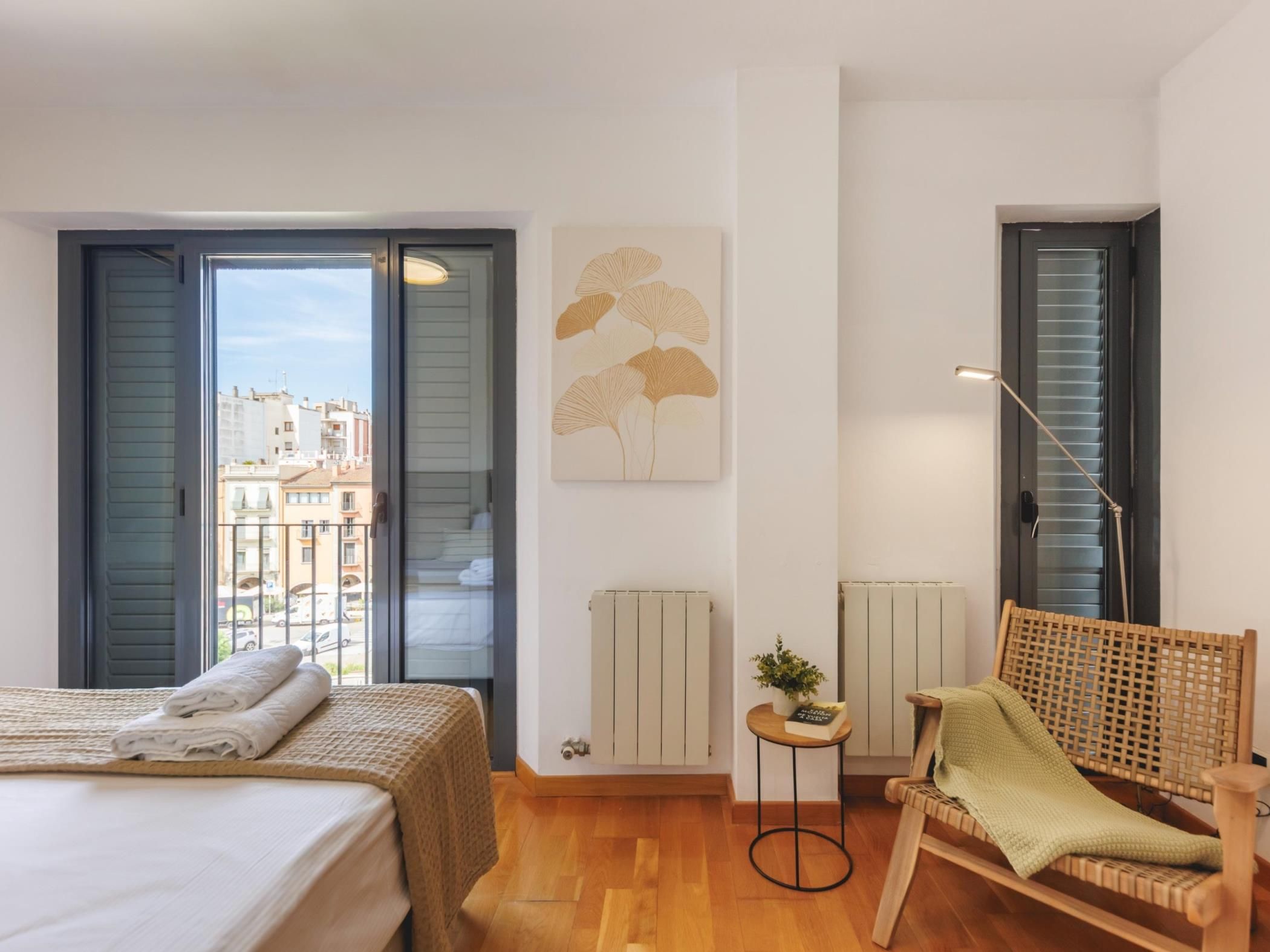 A bedroom with a bed, a chair, a radiator, a window, and a view of buildings outside.