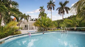 Una piscina con superficie de agua azul cristalina, rodeada de palmeras y una zona de estar cubierta.