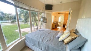 Un dormitorio con una cama grande, vistas al exterior y una zona de comedor al fondo.