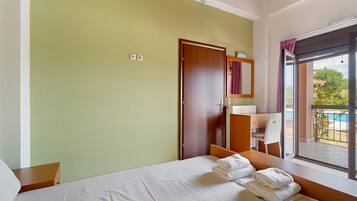 A hotel room with a bed, a desk, a chair, a window with a view, and a door.