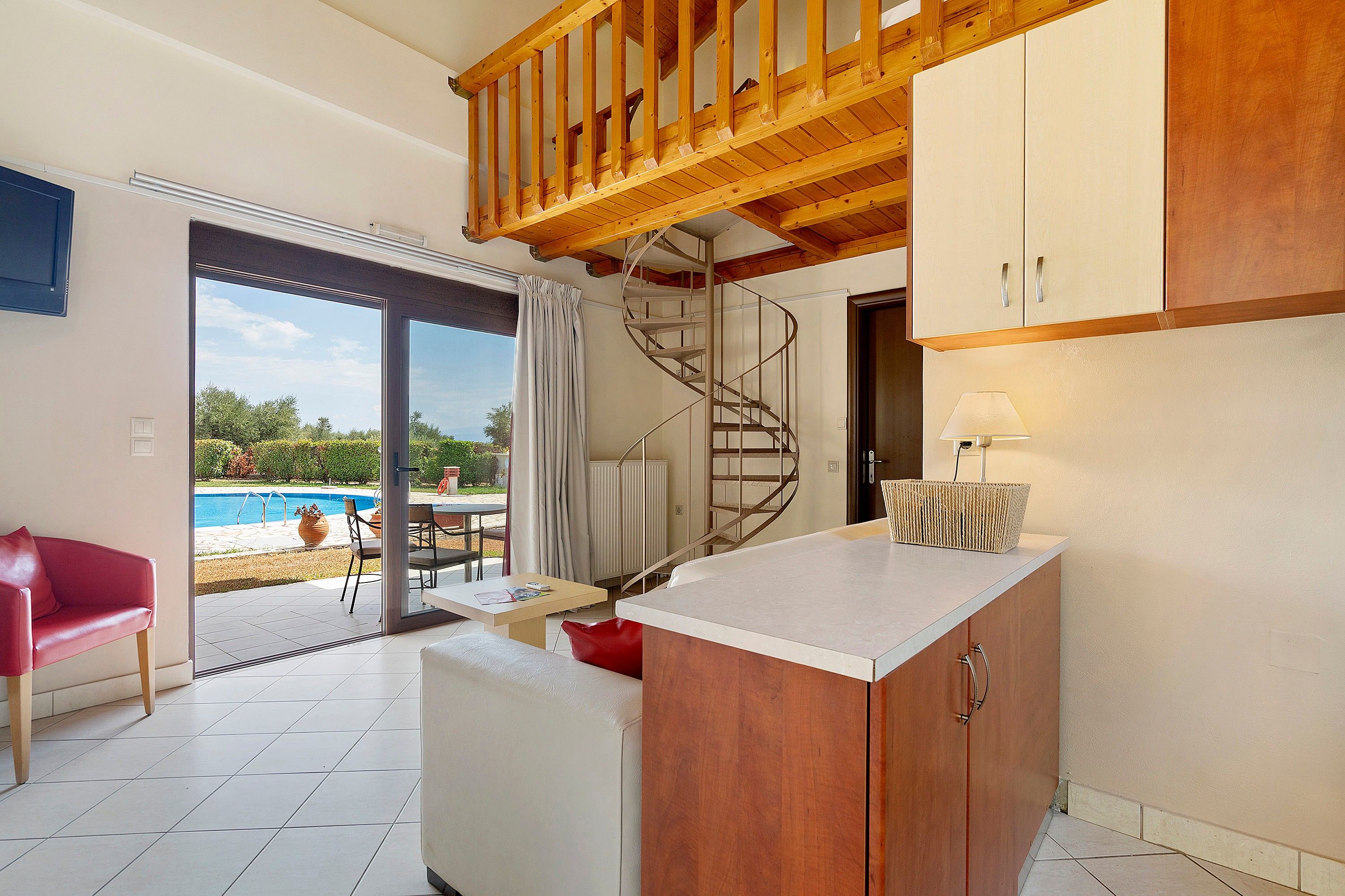 A compact kitchen with a wooden ceiling, a spiral staircase, and a view of a swimming pool outside.