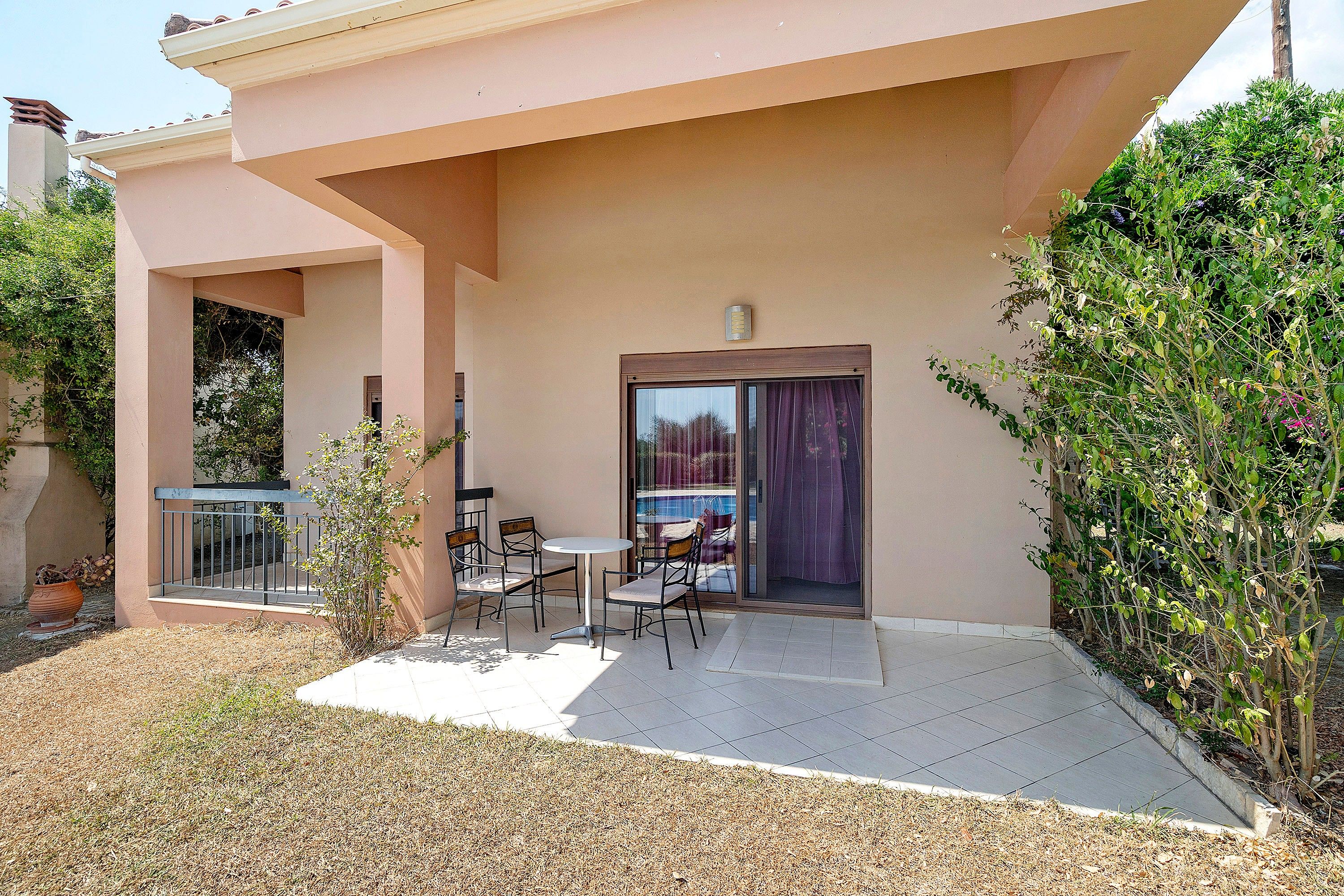 Un bâtiment doté d’un patio comprenant une table et des chaises, un petit jardin et une porte donnant accès à un espace intérieur.
