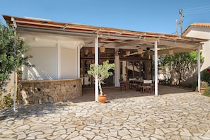 A covered outdoor patio with stone flooring, a potted tree, and a table with chairs. - Villa 'Ariadni' in Marathiás (Marathiás)