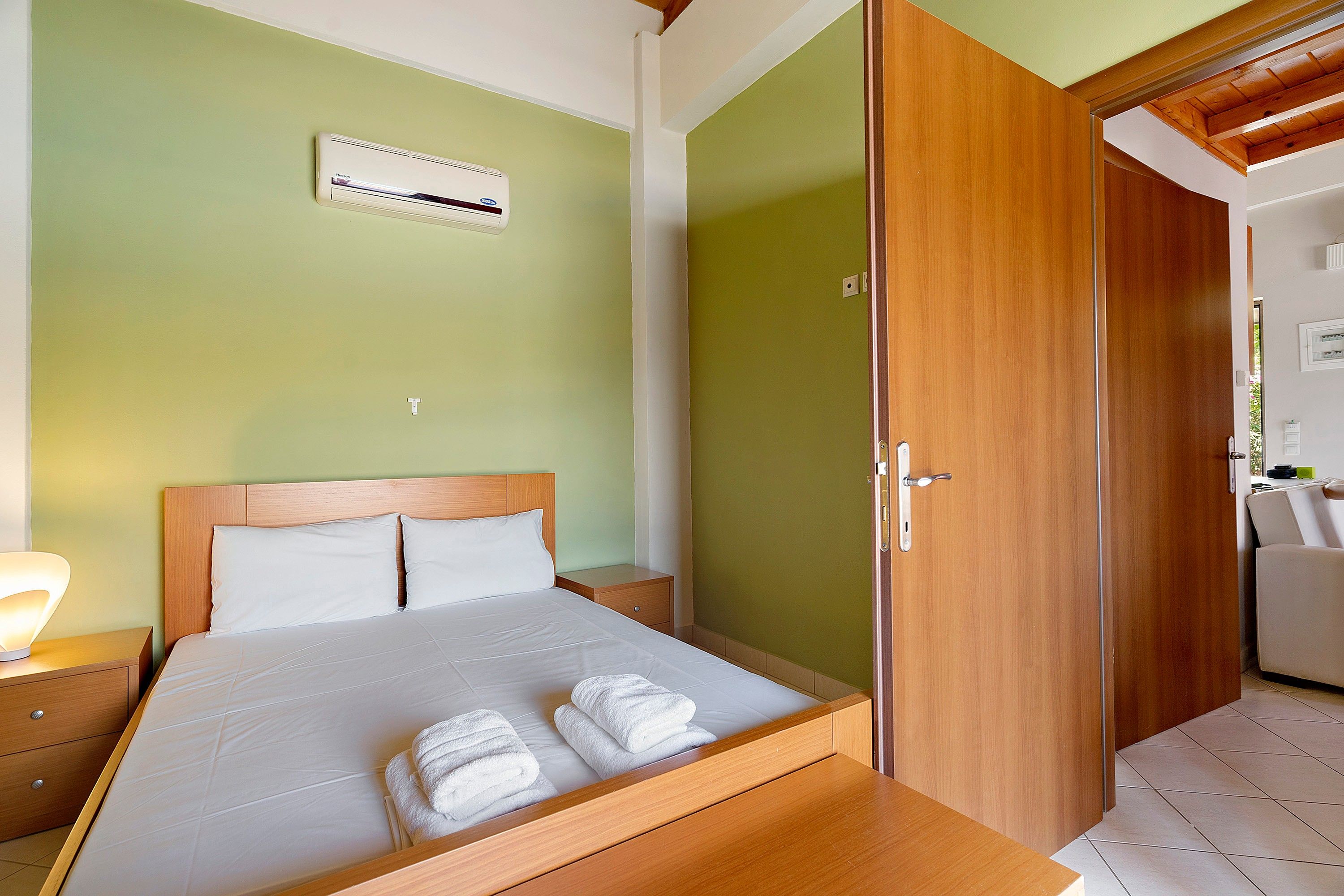 A hotel room with a bed, a nightstand, a wooden wardrobe, and a bathroom visible through an open door.