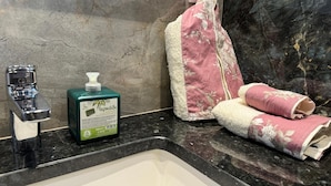 A bathroom with a marble sink, a green bottle of hand soap, and a pink towel.