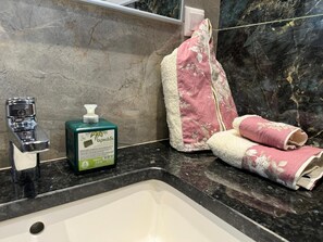 Une salle de bain avec un lavabo en marbre, un flacon de savon liquide vert et une serviette rose.