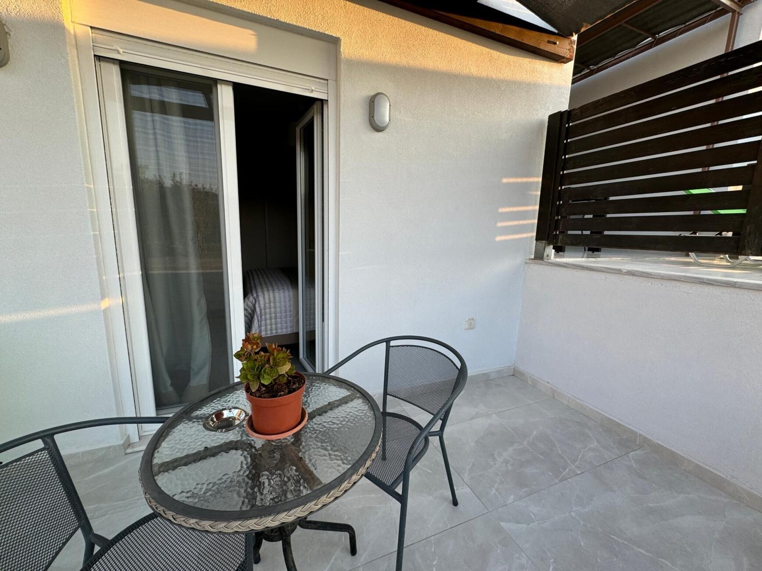 A glass-top table with a potted plant, two chairs, and a sliding glass door leading to an interior space.