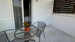 A glass-top table with a potted plant, two chairs, and a sliding glass door leading to an interior space.