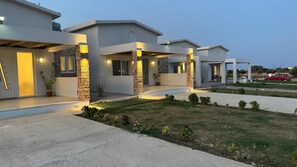 A modern residential building with a covered porch area, a well-maintained lawn, and a red car parked in the driveway.