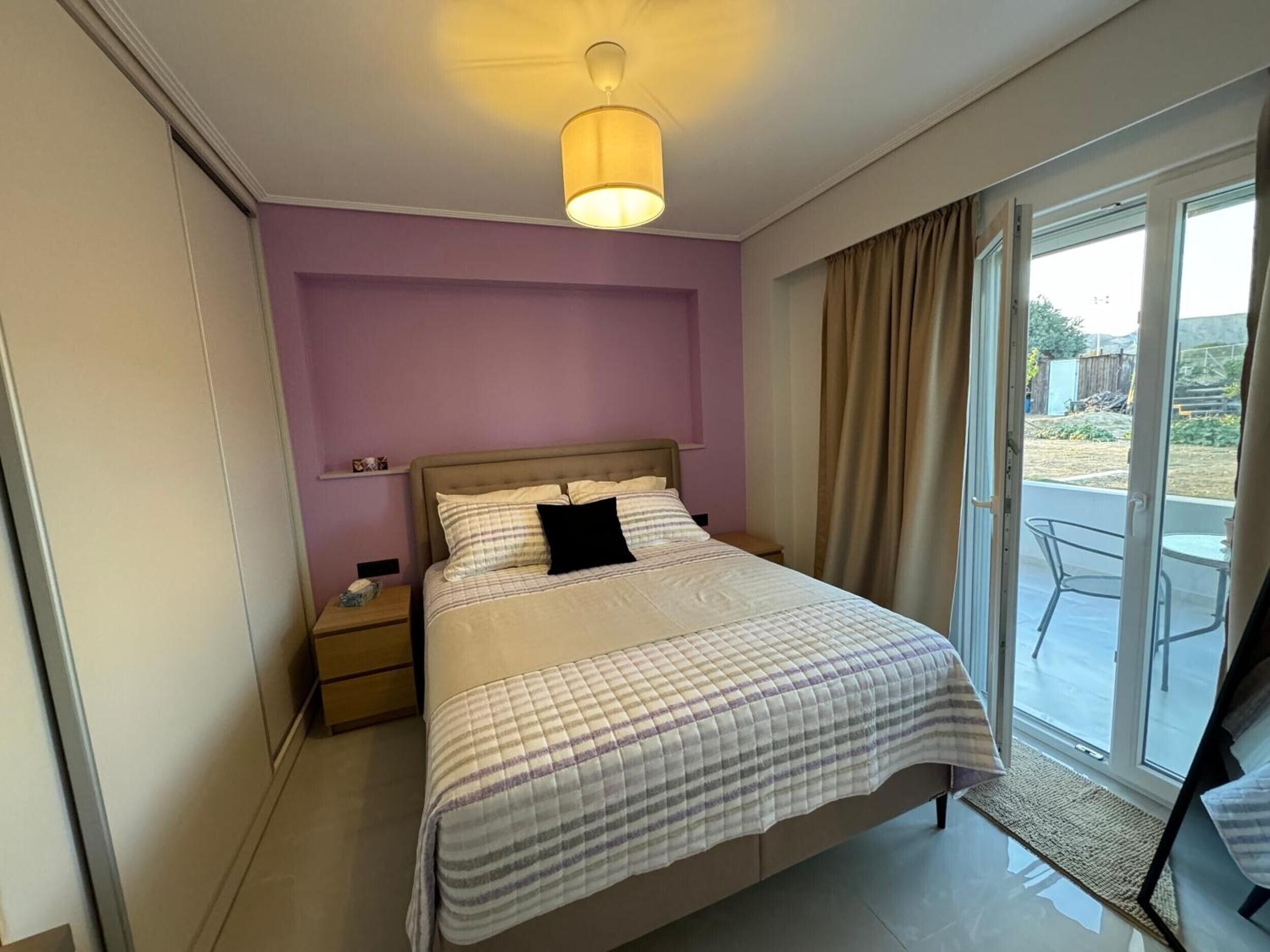 A bedroom with a bed, a nightstand, a lamp, and a view of the outdoors through a sliding glass door.