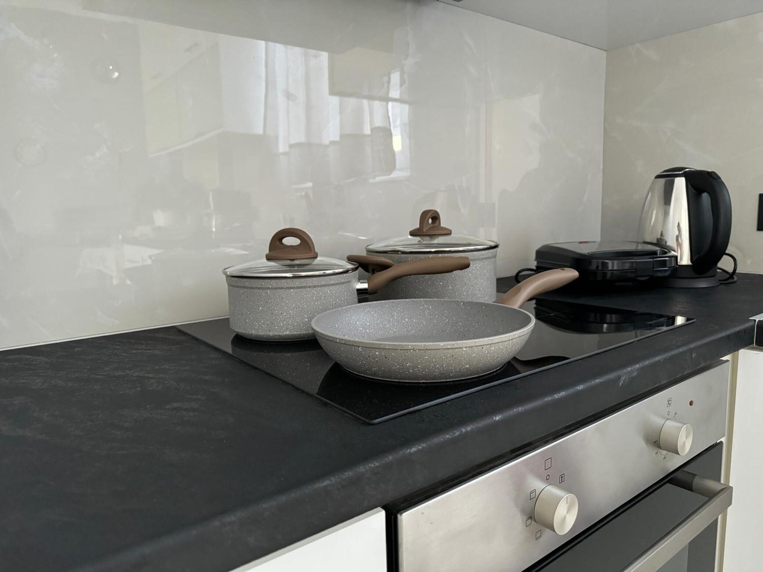 Cozinha com bancada preta, chaleira, frigideira e dois panelas com tampas.