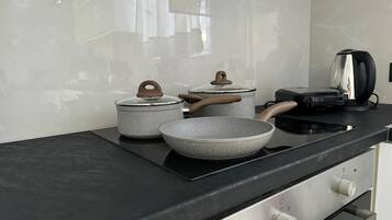 Cozinha com bancada preta, chaleira, frigideira e dois panelas com tampas.