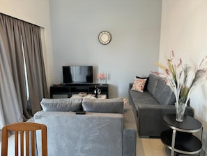 A modern living room with a flat-screen TV, grey sofas, a small round table, and a decorative vase with plants.