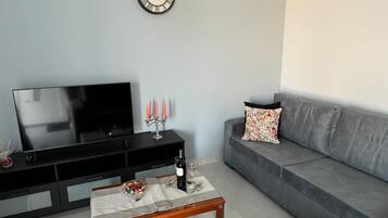 Ein Wohnzimmer mit einem Flachbildfernseher, einem Holztisch mit einer Glasvase, einer Weinflasche und einem Kandelaber.