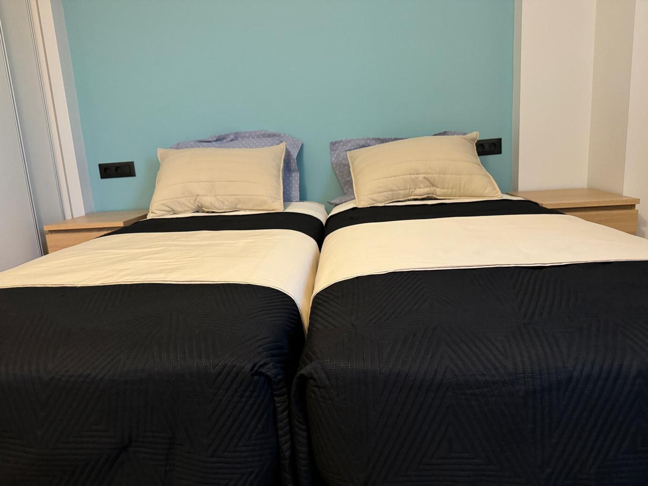 En dobbeltseng med sort og beige dynebetræk, to puder og et natbord med en lampe.