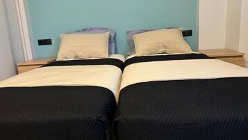 En dobbeltseng med sort og beige dynebetræk, to puder og et natbord med en lampe.
