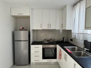 A compact kitchen with white cabinets, a stainless steel refrigerator, a built-in oven, and a black countertop.