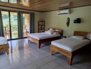 A room with two wooden beds, a tiled floor, an air conditioning unit, and a view through a glass door to an outdoor area. - Cecropia Wild Corcovado - Villa de 1 dormitorio 1 (Osa)