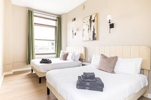 Ein Hotelzimmer mit zwei Betten, einem großen Fenster mit Vorhängen, einem Gemälde an der Wand und einer Lampe.