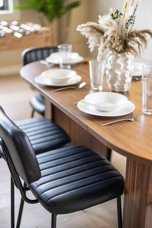 Een eettafel met stoelen, borden en een vaas met gedroogde bloemen.
