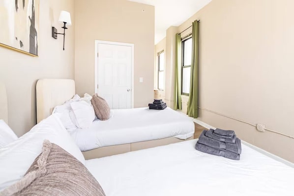 Een hotelkamer met twee bedden, een deur, een raam met gordijnen en een wandlamp.