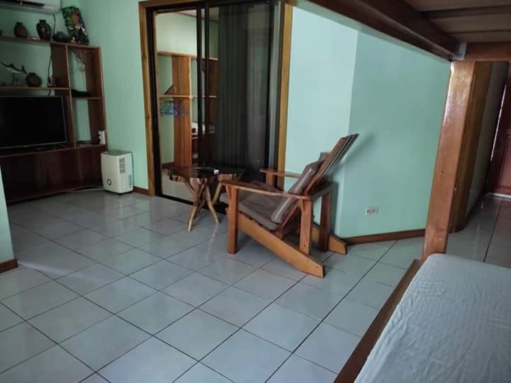 Quarto com cama, uma cadeira de madeira, uma mesinha, televisão e um armário.