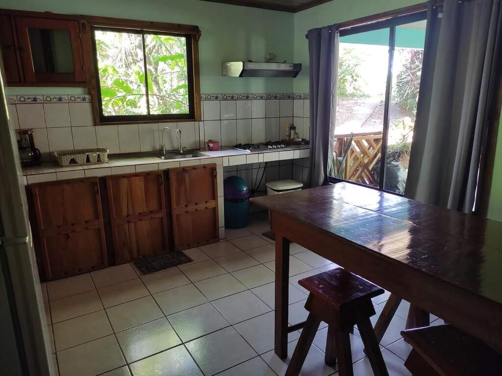A kitchen with a tiled backsplash, wooden cabinets, a sink, and a window with a view of greenery.