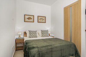 Ein Schlafzimmer mit einem Bett, zwei an der Wand befestigten Fischbildern, einem Holzschrank und einem Nachttisch mit Lampe.