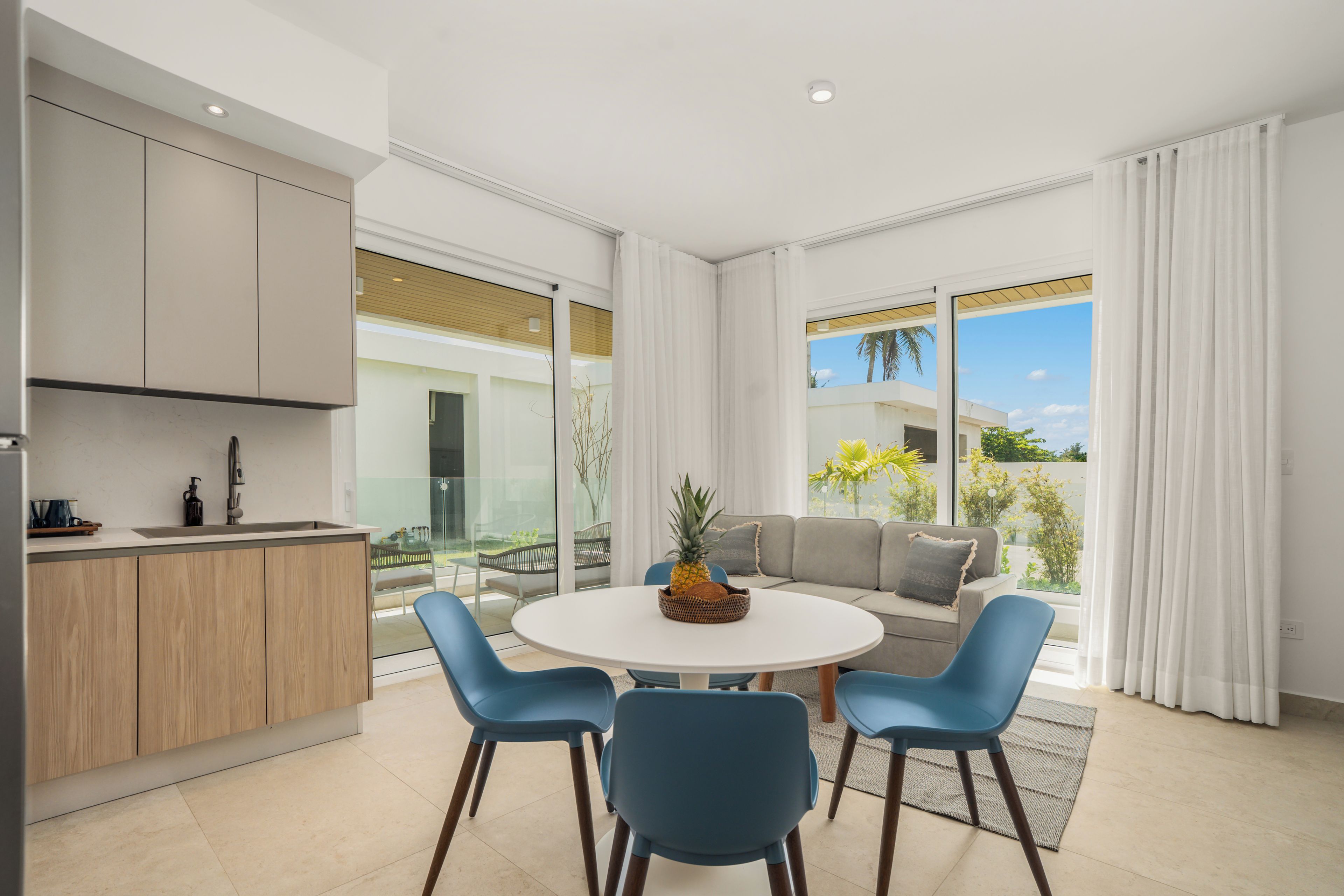 A modern kitchen with a dining area, a sofa, and a view of the outdoors.