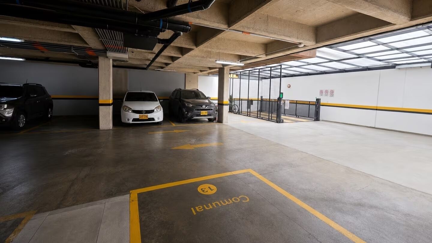 Un estacionamiento con varios niveles, pisos de concreto, líneas de estacionamiento amarillas y algunos coches aparcados.