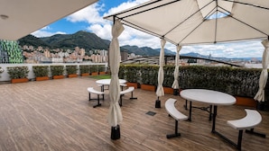 Una terrazza esterna con tavoli e sedie, vista su un panorama urbano e montagne sullo sfondo.
