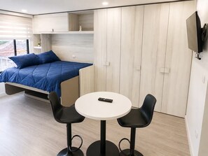 A modern room with a bed, a small table, two chairs, and a TV mounted on the wall. - Modern Studio in Chapinero | City Views & Workspace (Bogotá)