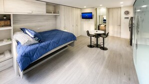 Una camera da letto moderna con un letto, una televisione, un piccolo tavolo con sedie e un armadio a muro.