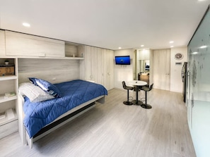 A modern bedroom with a bed, a TV, a small table with chairs, and a built-in wardrobe. - Modern Studio in Chapinero | City Views & Workspace (Bogotá)