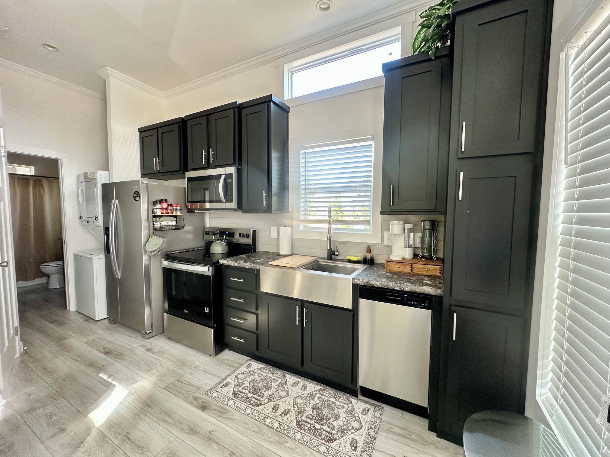 A modern kitchen with dark cabinets, stainless steel appliances, and a window with blinds.