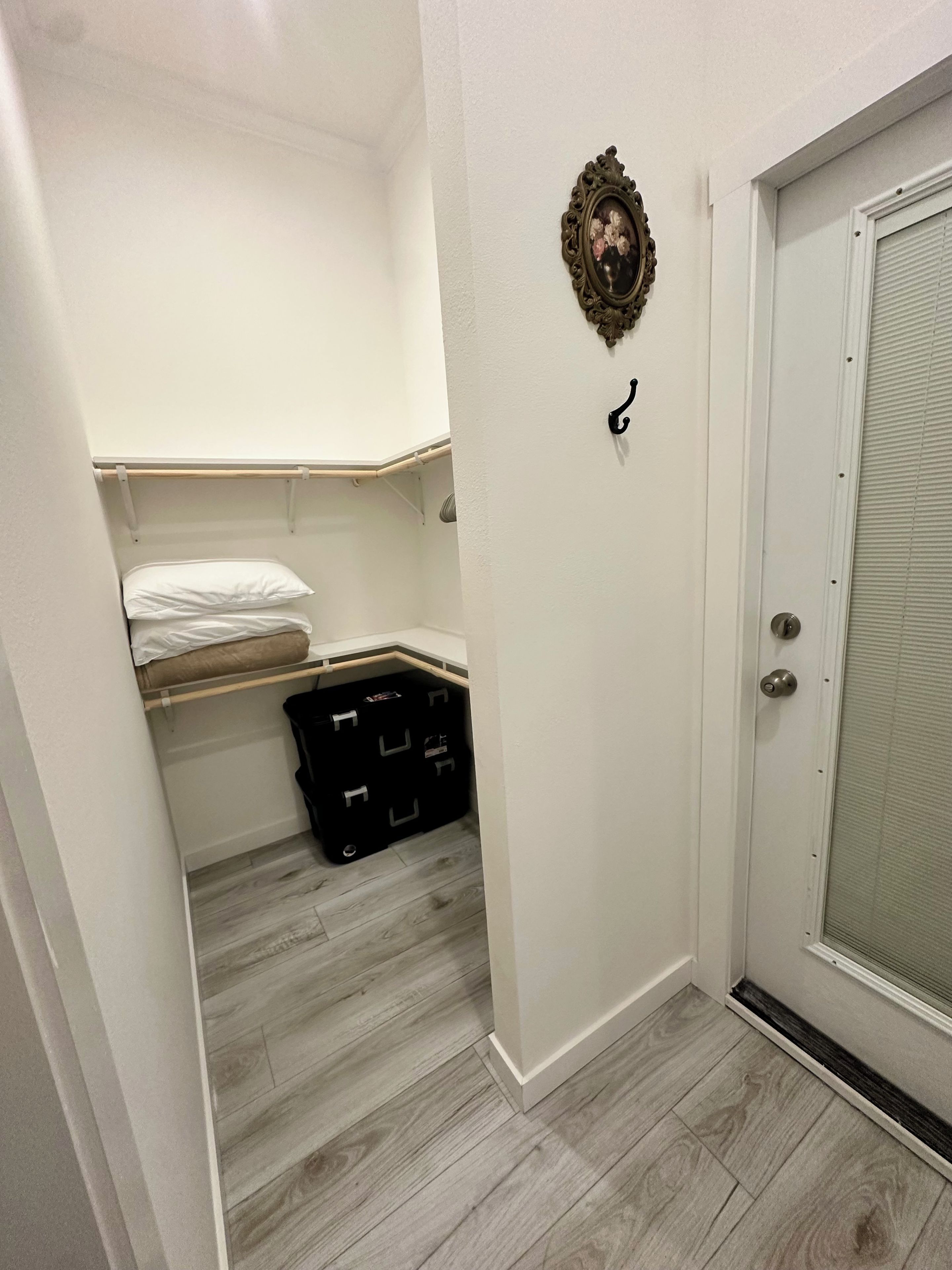 A narrow hallway with a white door, a black storage box, and a white shelf with a pillow.