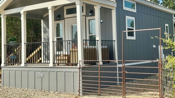 Ein eingeschossiges Haus mit einer Veranda, einem umzäunten Garten und einem Metalltor.