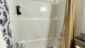 A bathroom with a shower, toilet, and a small table with a towel.