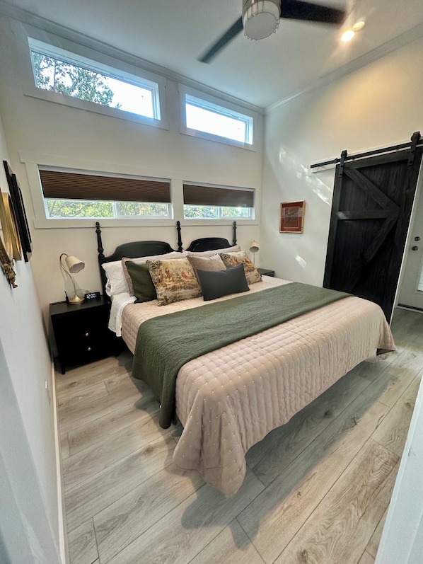 Une chambre à coucher comprenant un lit, une table de chevet, une horloge murale et un ventilateur de plafond.