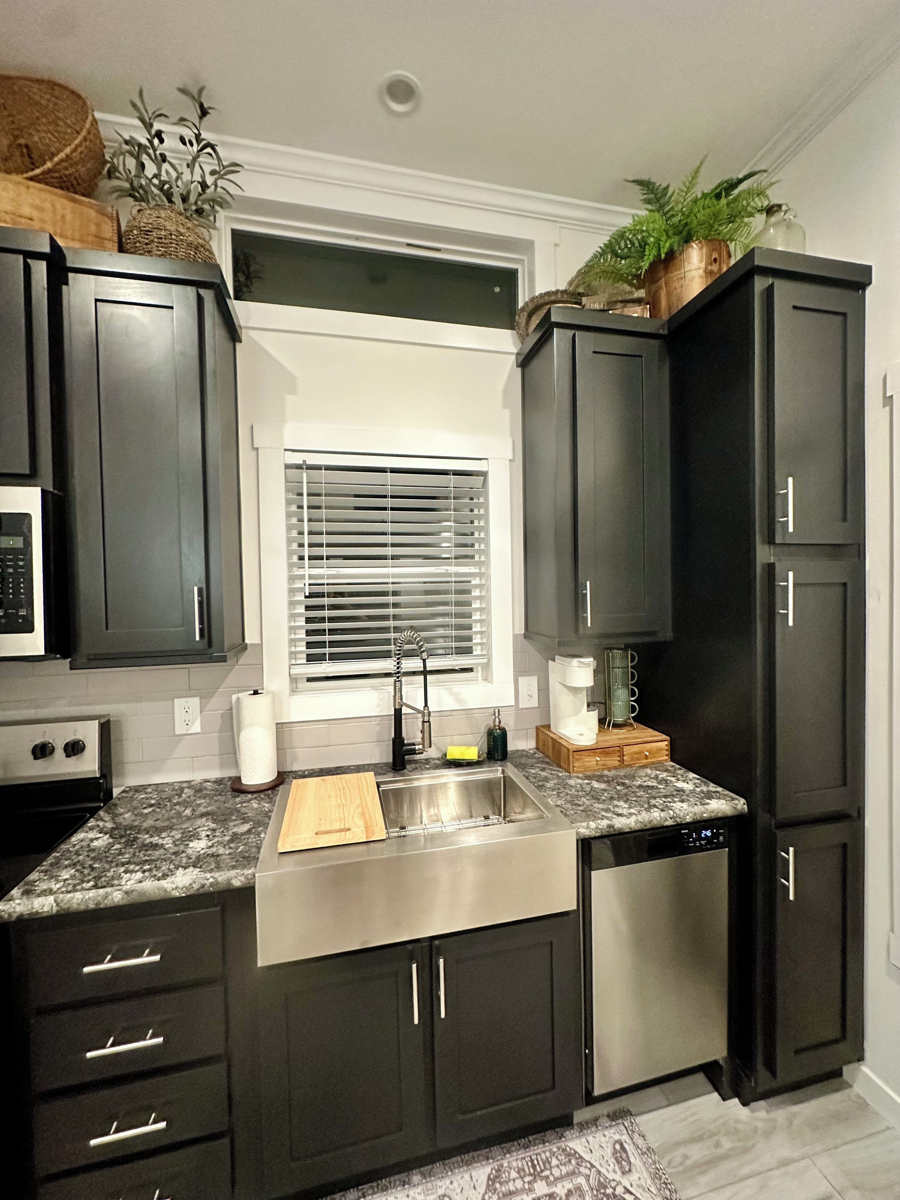 A modern kitchen with dark cabinetry, a stainless steel sink, and a built-in dishwasher.