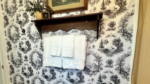 Ein Badezimmer mit einem gemusterten Wandpapier, einem gerahmten Bild über einem Handtuchhalter und einem kleinen Tisch mit einem Handtuch.