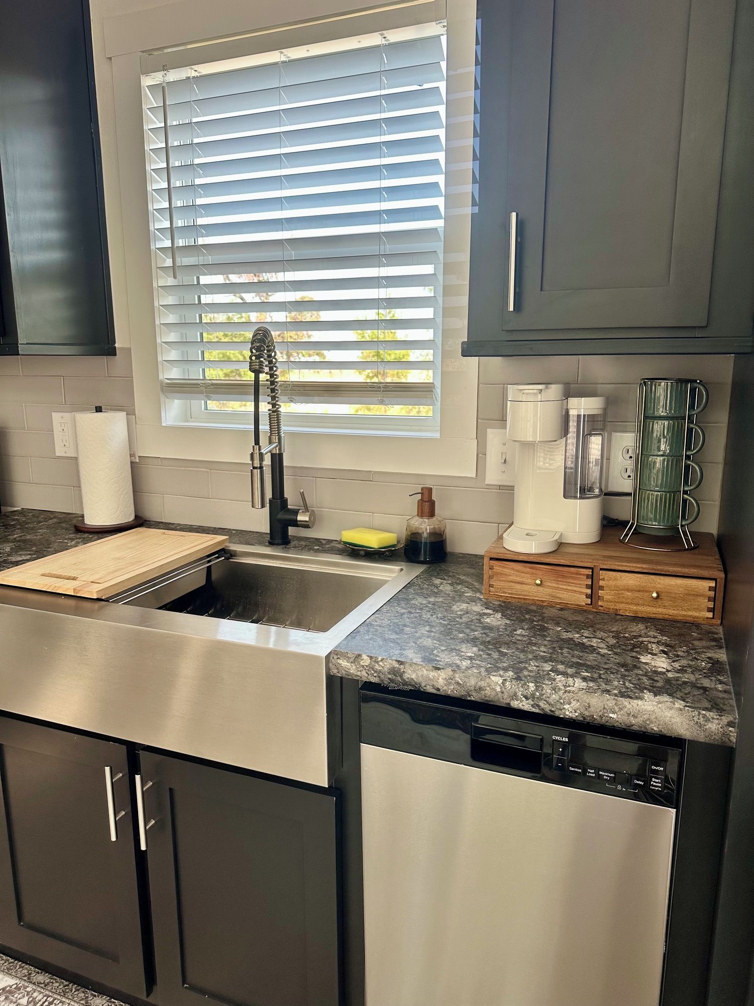 A kitchen with a stainless steel sink, a dish soap bottle, a paper towel holder, and a coffee maker.