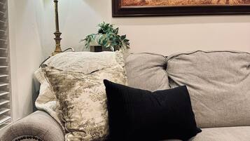 A living room with a beige sofa, a black pillow, a lamp, and a framed landscape painting on the wall.